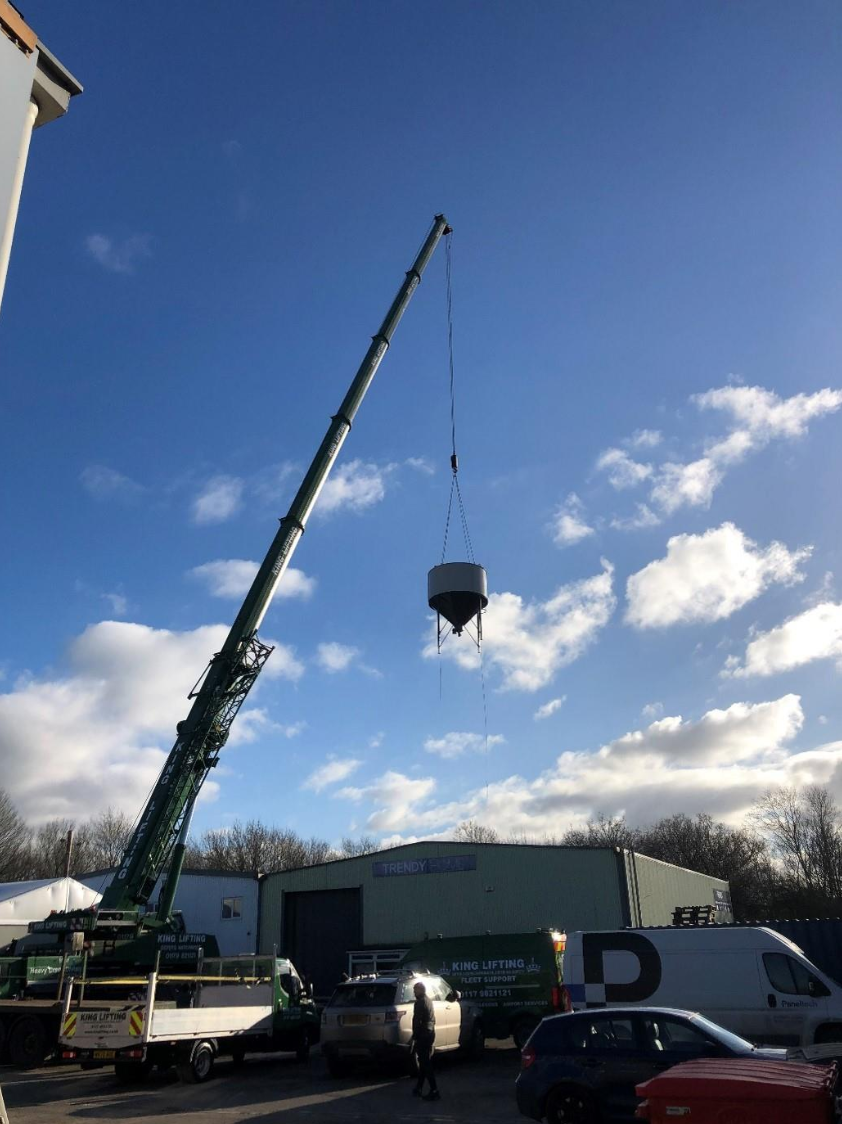 A C25 Industrial Wood Waste Silo being lifted over Paneltech’s factory using a 200-tonne crane during installation. The clear blue sky and industrial setting highlight the scale of the operation.