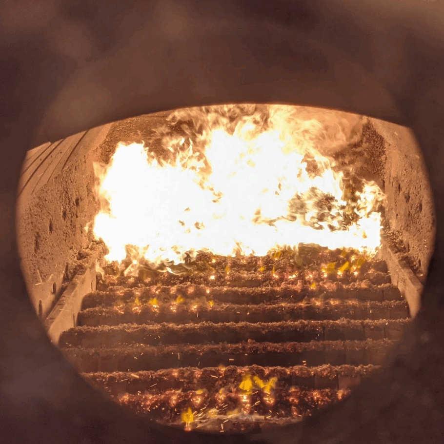 Combustion chamber of Ranheat M19 industrial biomass boiler with chipboard dust fuel igniting on ceramic step grate.