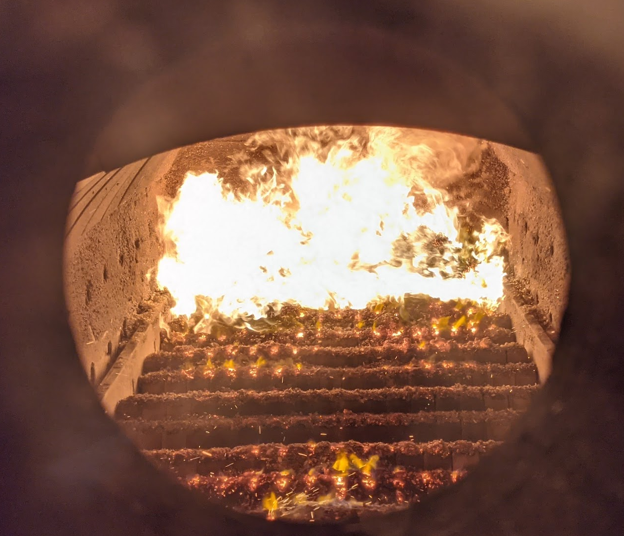 Combustion chamber of Ranheat M19 industrial biomass boiler with chipboard dust fuel igniting on ceramic step grate.